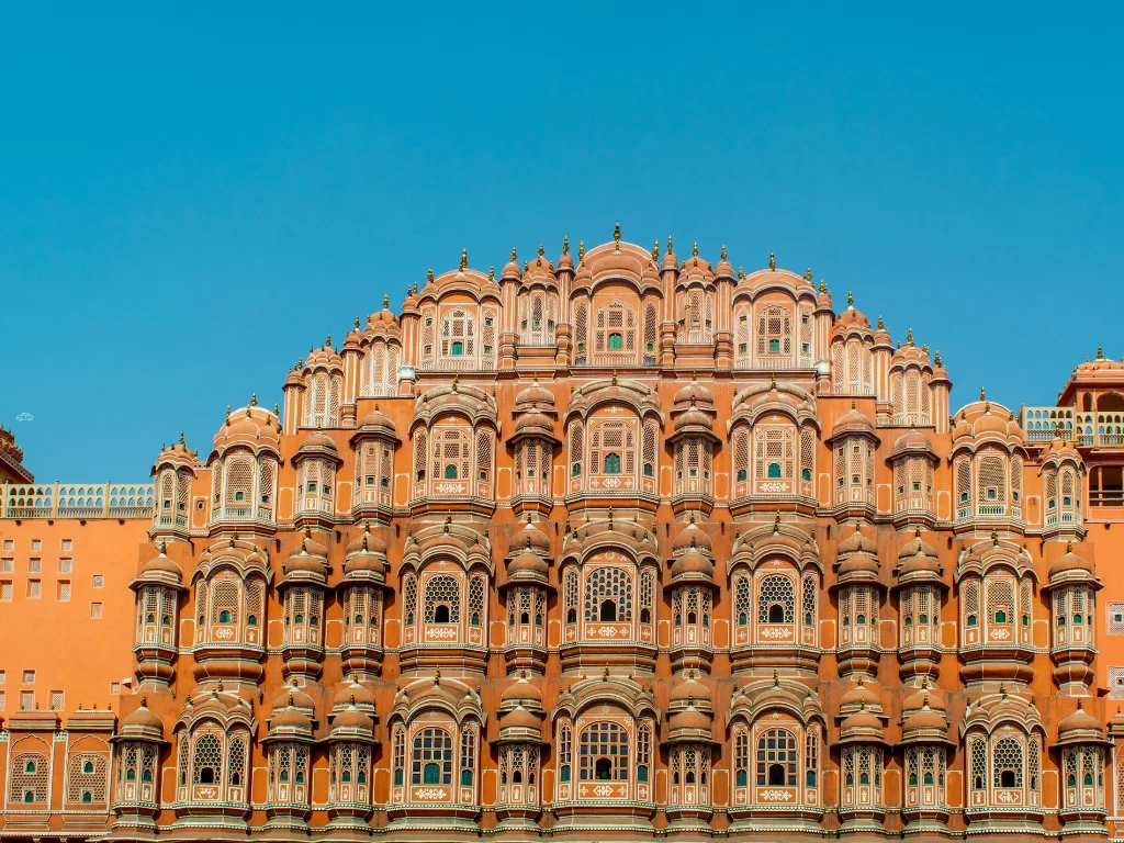 Hawa Mahal facade Jaipur clear day, featuring pink honeycomb windows arches blue sky, perfect romantic experience Rajasthan tour packages.