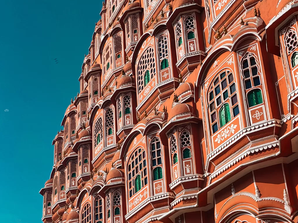 Hawa Mahal side view Jaipur blue sky, featuring pink jharokhas green shutters arches, perfect romantic experience Rajasthan tour packages.