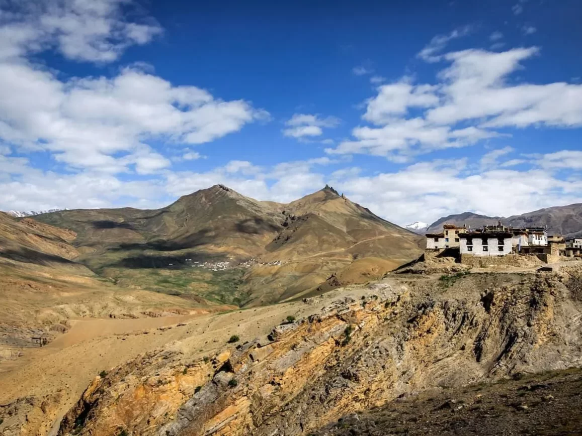 Hikkim Village Spiti near Kaza during partly cloudy skies, featuring white monastery rocky brown hills snow peaks valley views, perfect cultural experience Himachal tour package.