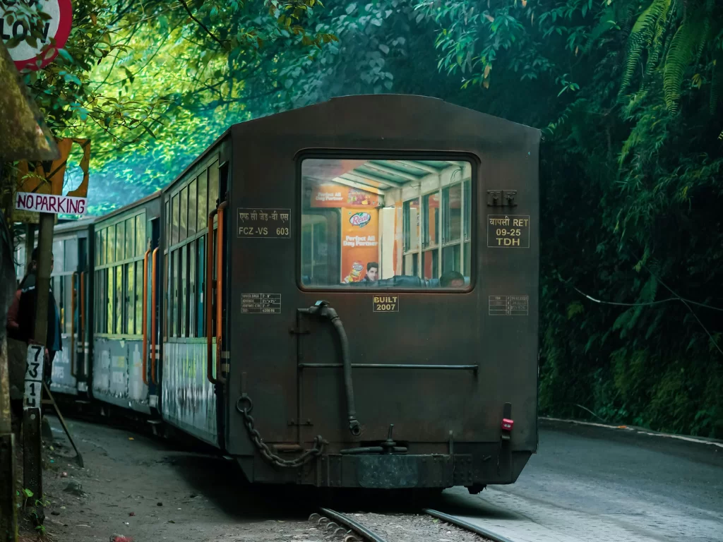 Darjeeling Himalayan Railway toy train coach passing through forested track during daytime, featuring vintage carriage and lush greenery, perfect scenic Sikkim tour package