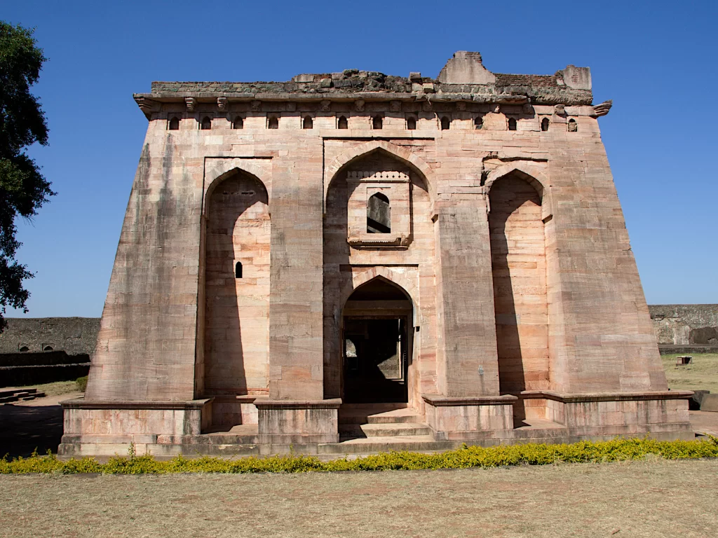 Mandu tower ruins under clear skies, featuring three-arched pink stone facade, perfect heritage experience with Madhya Pradesh tour packages.