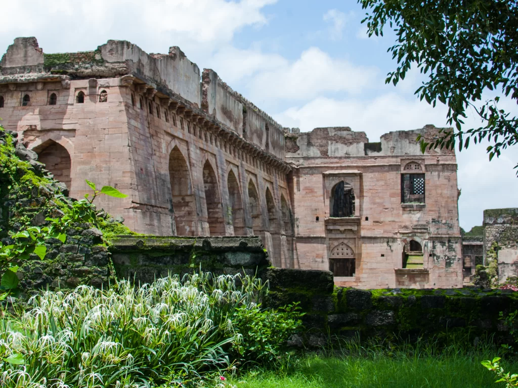 Hindola Mahal at Mandu under partly cloudy skies, featuring sloping walls with multiple arched facade, perfect heritage experience with Madhya Pradesh tour packages.