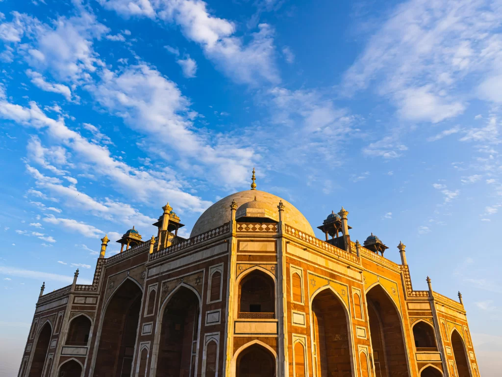 Humayun’s Tomb, Delhi – close-up low-angle view of the Mughal red sandstone mausoleum with white marble dome and arches under a bright blue sky, iconic UNESCO World Heritage monument.