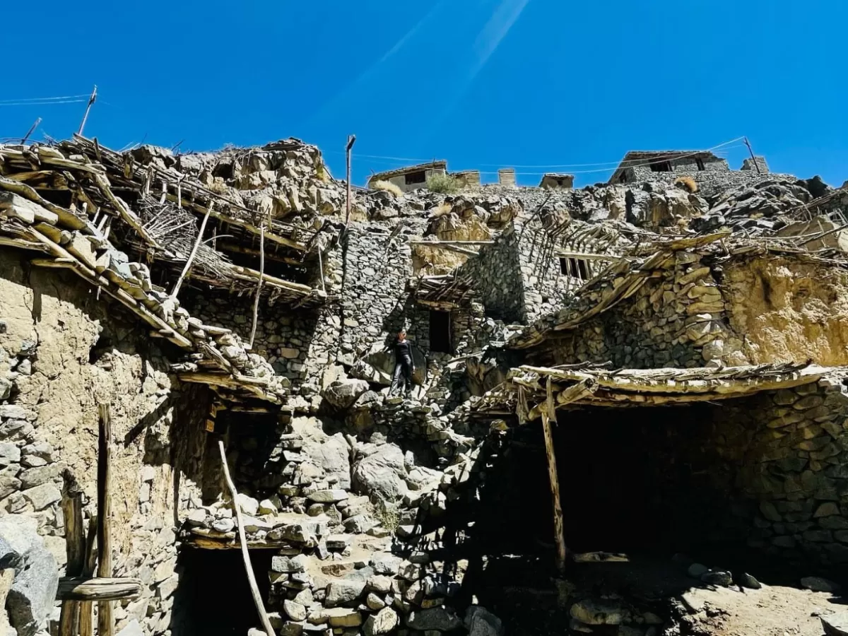 Hunderman Village Kargil Ladakh closeup abandoned stone houses with wooden ladders on sheer cliff face, explorer silhouette amid crumbling Brokpa architecture, barren rocky mountains under clear blue skies, perfect LoC adventure India tour package.