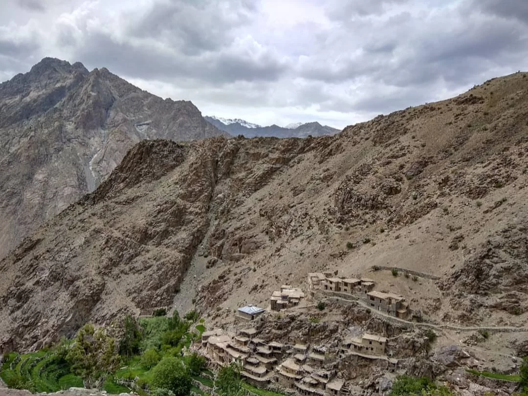 Hunderman Village Kargil Ladakh ghost settlement terraced on dramatic sheer cliff face under moody overcast skies, Brokpa stone houses amid rugged Karakoram peaks with distant snow, perfect LoC adventure India tour package.