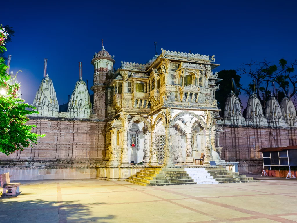 Ornate gateway at Hutheesing Jain Temple Ahmedabad during night, featuring illuminated shikharas and carved walls, perfect cultural Gujarat tour package.