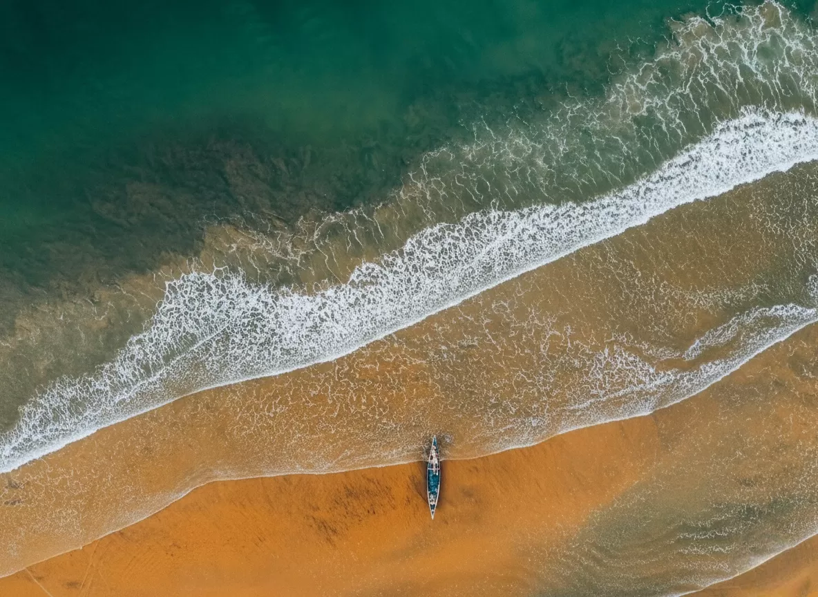 Varkala Beach Kerala aerial beached boat orange sands turquoise Arabian Sea, crashing waves green waters serene coastline, perfect Kerala fishing boat beach package. 