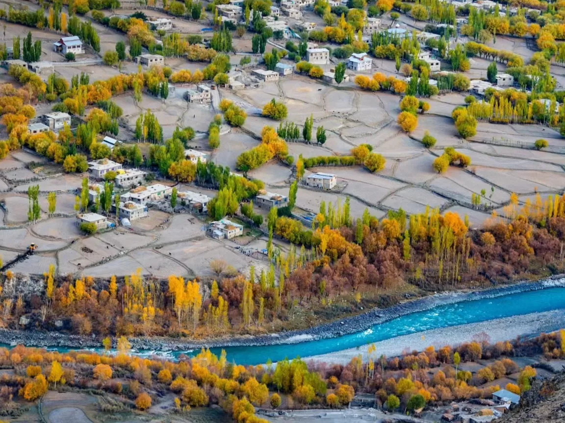 Autumn village aerial at Kargil City during autumn, featuring yellow trees, terraced fields, blue river, perfect cultural experience with Ladakh Kargil tour package.