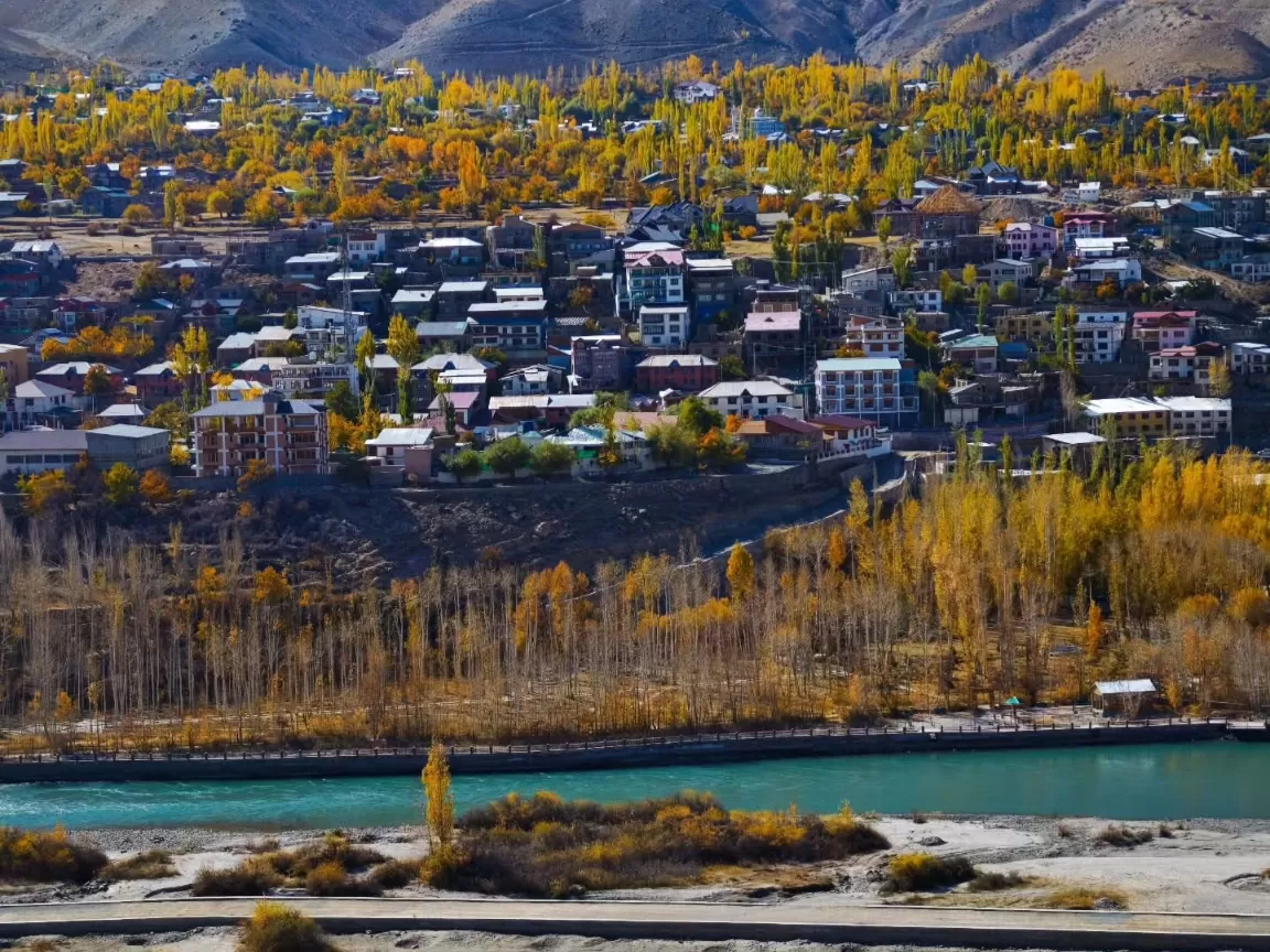 Autumn cityscape at Kargil City during golden hour autumn, featuring yellow trees, colorful houses, turquoise river, perfect cultural experience with Ladakh Kargil tour package. 