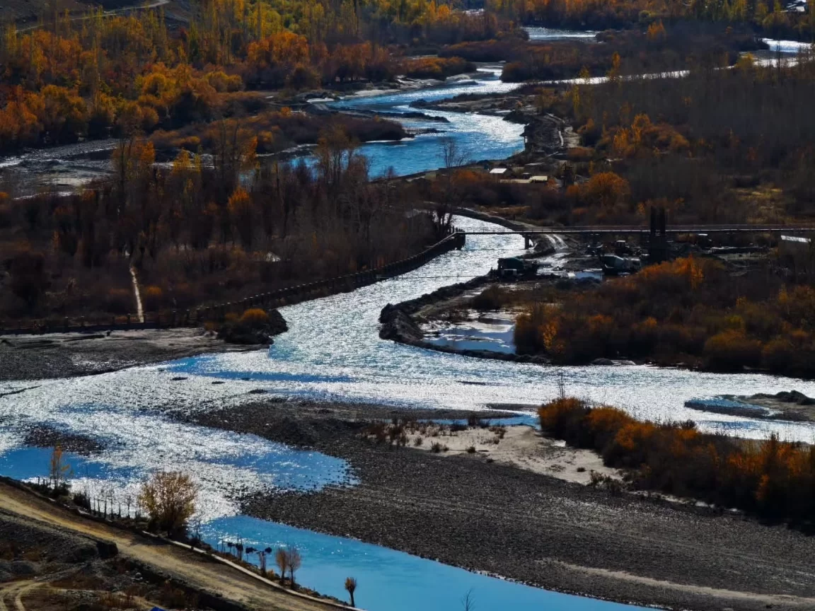 Autumn river valley at Kargil City during golden hour autumn, featuring yellow trees, winding blue river, bridges, perfect adventure experience with Ladakh Kargil tour package.