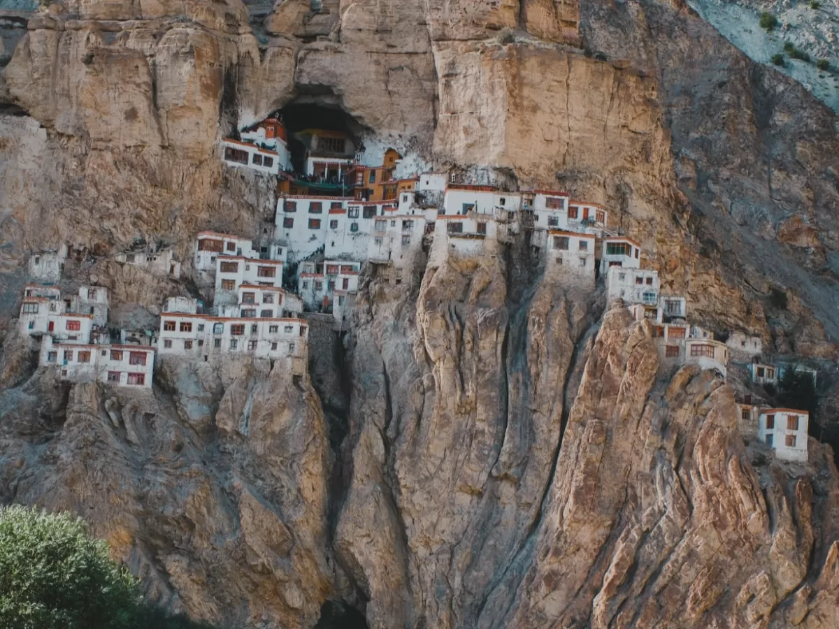 Zanskar Ladakh Phuktal Phugtal Gompa Buddhist cave monastery white buildings red roofs embedded rugged cliff cave entrance barren rocky Himalayan mountains landscape remote adventure trek pilgrimage tourism photography.