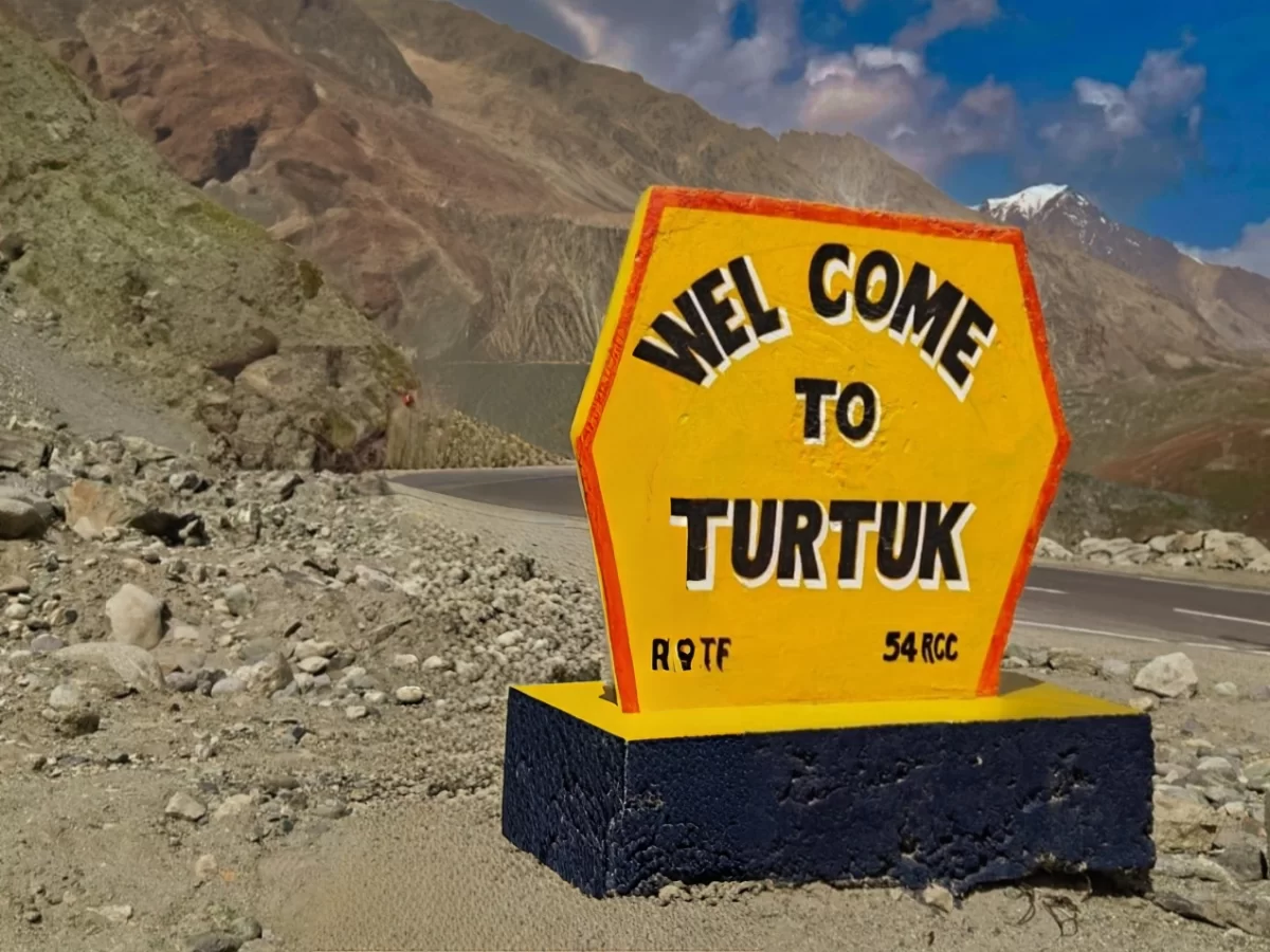 Welcome to Turtuk village signboard in Nubra Valley Ladakh during partly cloudy day, featuring R9TF unit marker, rugged mountains, perfect cultural Turtuk tour package. 