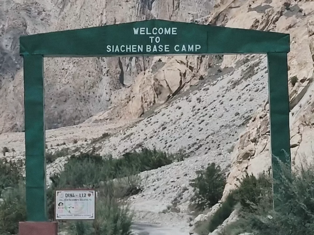 Welcome Siachen Base Camp green arch gateway Ladakh rugged rocky mountains greenery Dial 112 emergency sign military tourism entry point Nubra Valley Partapur Indian Army base adventure trek. 