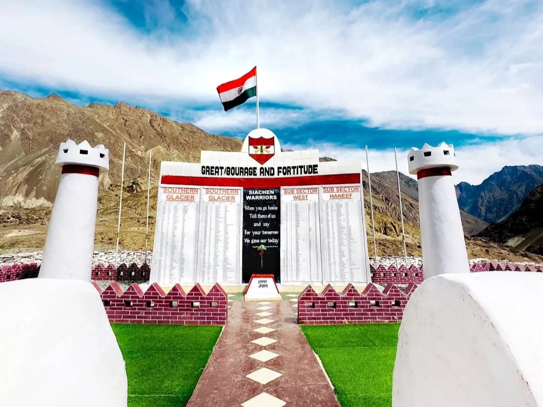 Great Courage Fortitude War Memorial Siachen Base Camp Ladakh white fort structure Indian tricolor flag martyr names Hindi English plaques turrets pathway grass Ladakh mountains military tribute tourism landmark.