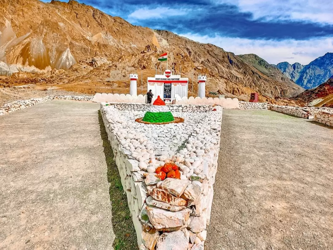 Siachen Base Camp white fort memorial structure Indian flag fluttering tricolor floral wreath saffron white green saffron marigolds pebble pathway rocky Ladakh mountains military tribute visitor viewpoint Nubra Valley.