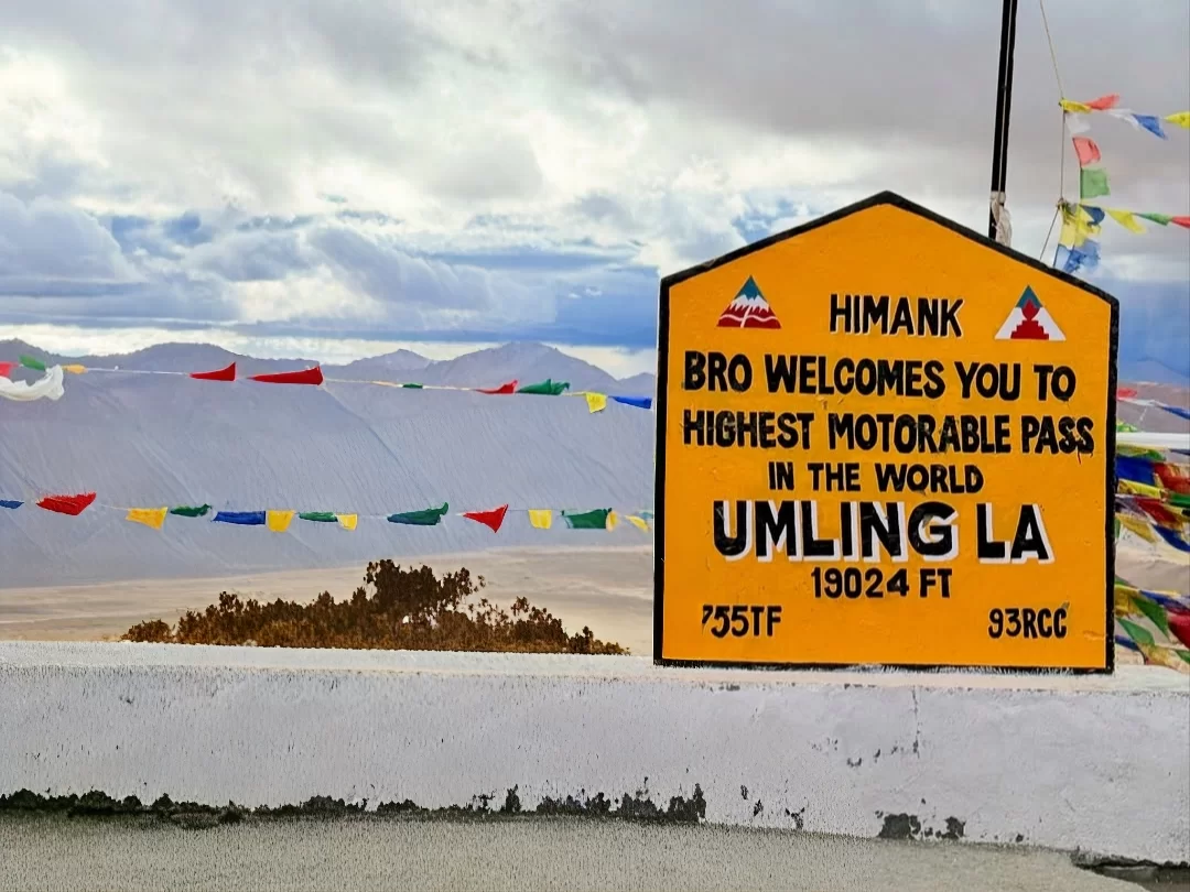 Umling La Ladakh BRO Himank signboard world's highest motorable pass 19300 ft prayer flags mountains, Changthang plateau adventure peak clouds, perfect Ladakh biking offroad expedition package.
