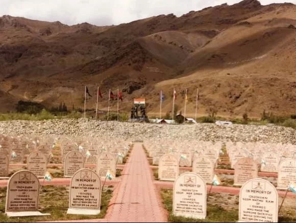 Drass Kargil War Memorial Ladakh vast white memorial headstones IN AF supreme sacrifice plaques red brick pathway multiple national flags rocky barren mountains backdrop, honoring 1999 Kargil heroes Operation Vijay NH1D Ladakh adventure trek.