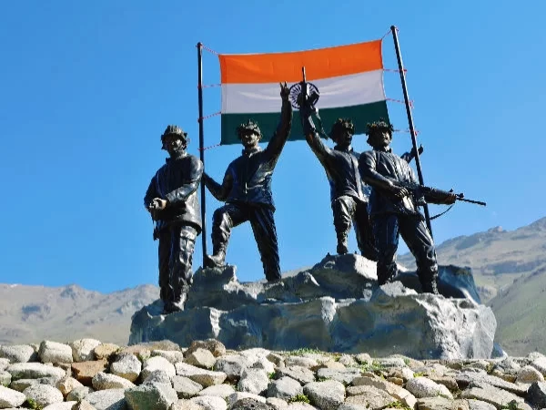 Drass War Memorial Ladakh soldiers statue Indian flag waving rifles helmets rocky base blue sky Kargil War heroes Operation Vijay tribute, perfect Ladakh heritage tour package.
