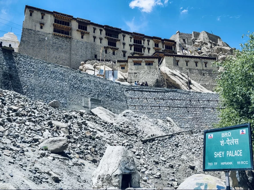 Ancient Shey Palace ruins in Ladakh under blue sky, featuring stone walls, signboard and rocky terrain, perfect Ladakh tour package.