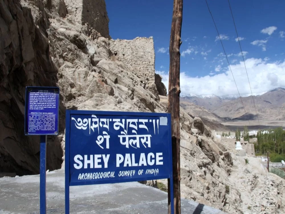 Shey Palace signboard and ruins in Ladakh during sunny day, featuring ASI plaques and mountain backdrop, perfect Ladakh tour package
