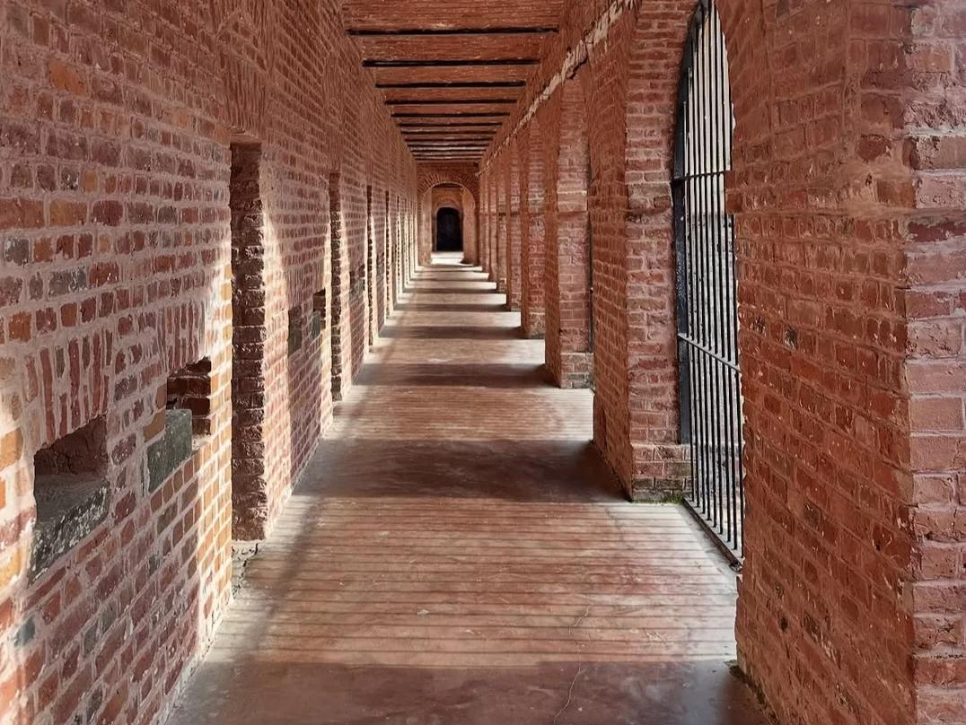 Cell corridor at Cellular Jail Port Blair Andaman during golden hour, featuring brick arches, iron bars, cell doors, shadows, perfect heritage experience Andaman tour package. 