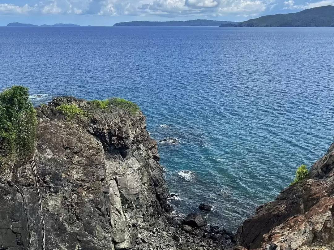 Ocean view at Chidiya Tapu Port Blair during partly cloudy day, featuring rocky cliffs, turquoise waves, lush greenery, distant islands, perfect sunset birdwatching adventure Andaman tour package