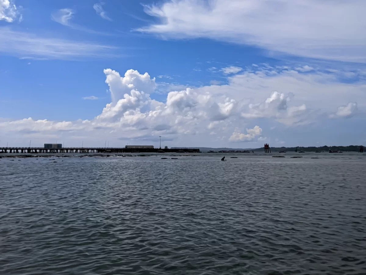 Bharatpur Beach port at Neil Island during sunny skies, featuring pier clouds sea horizon lighthouse, perfect romantic Andaman tour package.