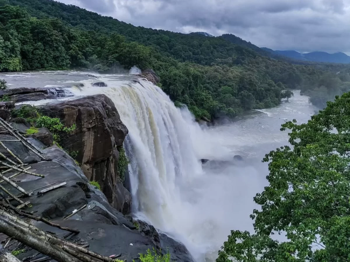 Athirappilly Waterfalls Thrissur Chalakudy Kerala India majestic powerful cascade plunging rocky cliff Chalakudy River lush green forested mountains misty spray cloudy skies foreground, perfect Kerala nature adventure wildlife tour package.