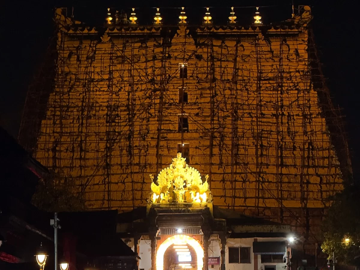 Sree Padmanabhaswamy Temple Thiruvananthapuram Kerala night illuminated golden nine-story gopuram scaffolding golden floral pinnacle entrance arch lights traditional buildings street lamps, Dravidian Vishnu Hindu temple tour package.