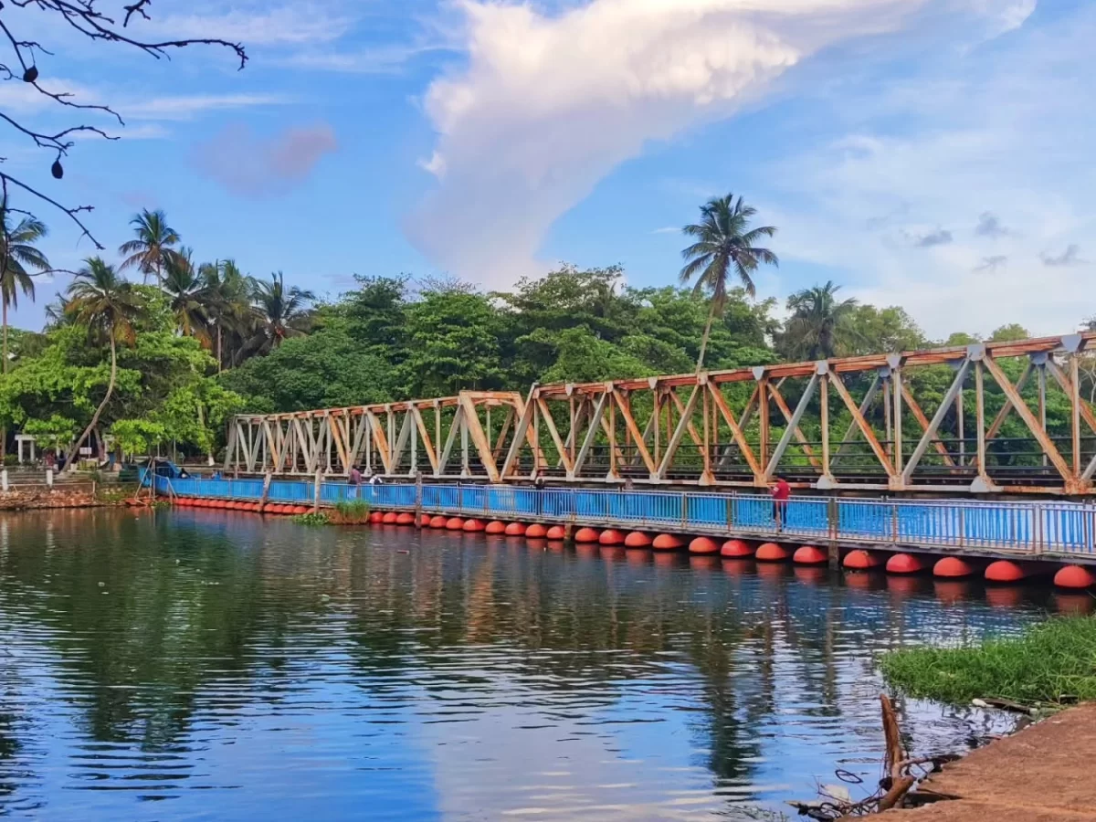 Thiruvananthapuram Kerala Veli Lake blue water reflection orange floating buoys wooden truss bridge palm trees green foliage cloudy blue sky serene backwater bridge scenic tour package