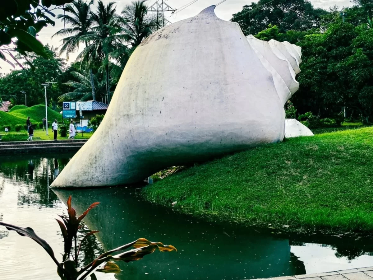 Thiruvananthapuram Kerala Veli Tourist Village Lake giant white conch shell sculpture landscaped garden green grass trees palm trees tourists pond reflection red flower plants iconic landmark tour package.