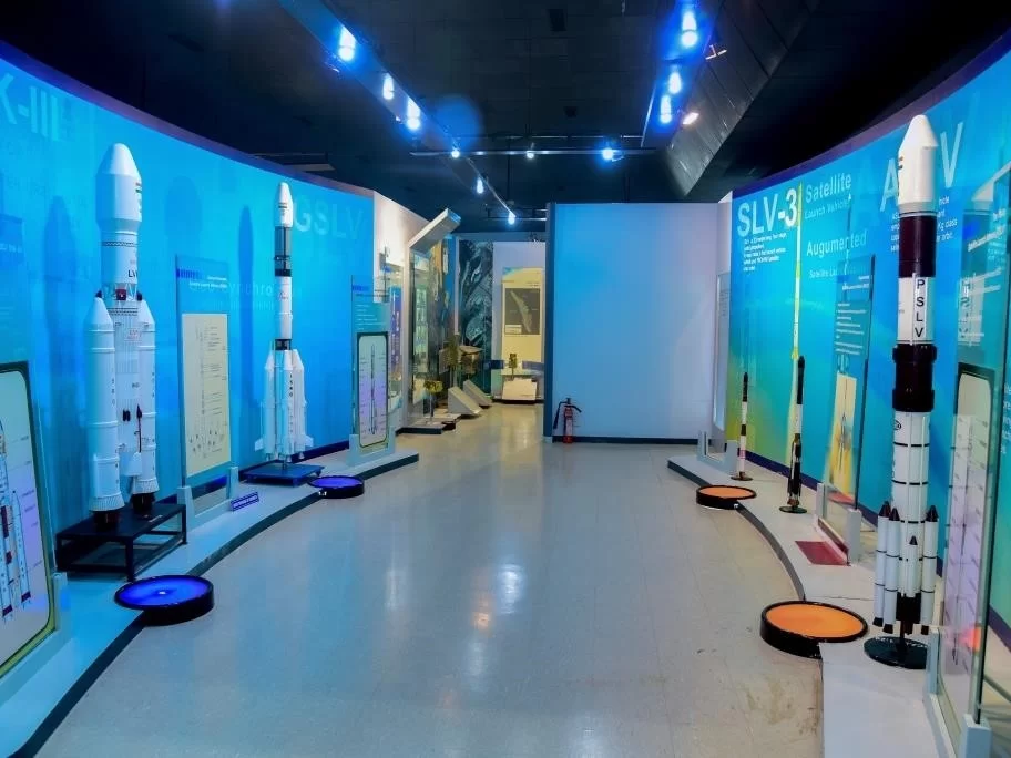 Vikram Sarabhai Space Centre Thiruvananthapuram ISRO museum interior GSLV SLV rocket models exhibits blue lighting display panels interactive screens curved walls LED floor lights educational gallery, space science tour package. 