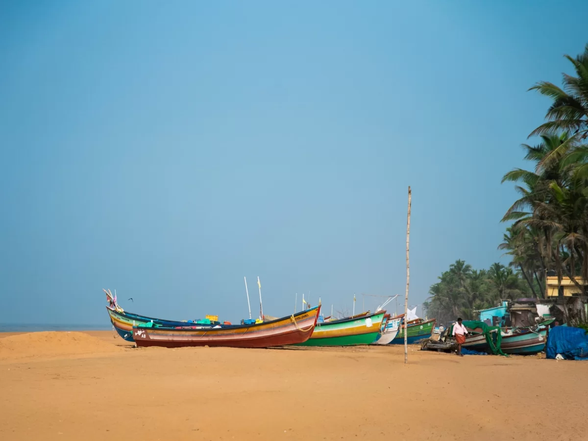 Thiruvananthapuram Kerala Thumba Beach golden sand row colorful traditional fishing boats red green yellow blue poles nets coconut palm trees clear blue sky serene coastal fishing village tour package.
