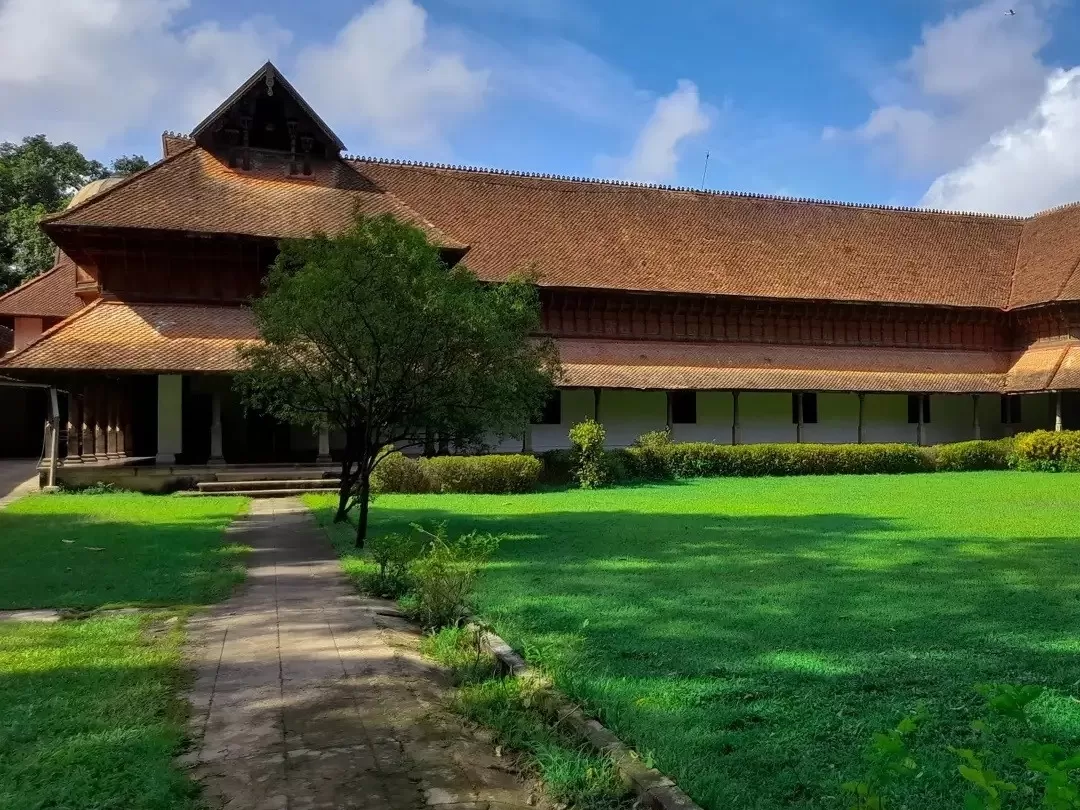 Kuthiramalika Palace Thiruvananthapuram Kerala side view showcasing classic Kerala nalukettu architecture with terracotta roofs, verandas, hedges and expansive green lawns, perfect India tour package.