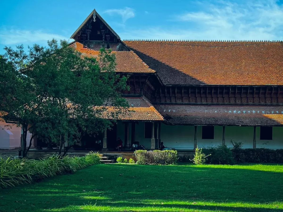 Kuthiramalika Palace Thiruvananthapuram Kerala elegant facade with terracotta roofs, carved wooden pillars, shaded verandas and well-kept green courtyard under blue sky, perfect India tour package. 