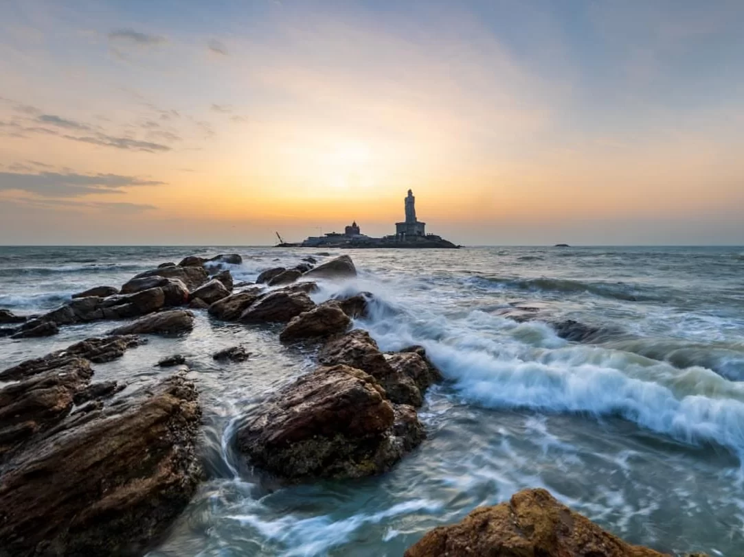 Triveni Sangam at Kanyakumari Beach during sunset, featuring Vivekananda Rock lighthouse and crashing waves, perfect Kanyakumari tour package.