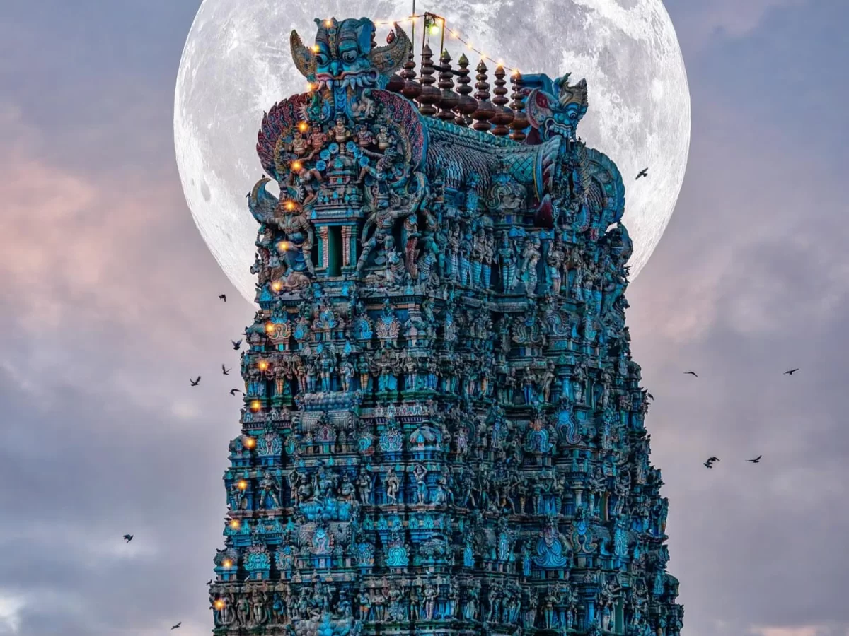 Meenakshi Amman Temple Madurai Tamil Nadu iconic 14-tiered gopuram tower in turquoise hues illuminated with oil lamps golden vimana crowning giant full moon twilight sky crows flying, mesmerizing Dravidian Hindu architecture spiritual tour package.