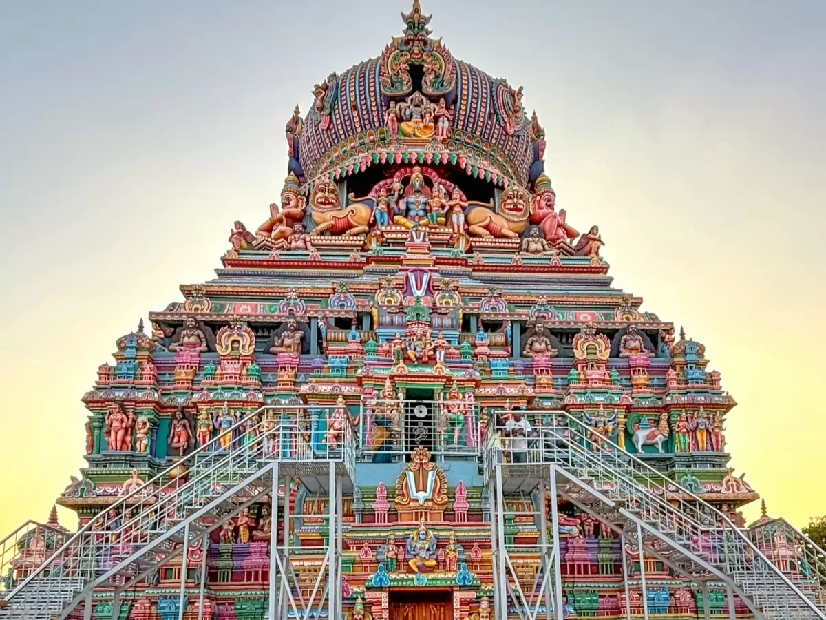Frontal view of Ashtanga Vimana Arulmigu Koodal Azhagar Temple Madurai Tamil Nadu during golden hour with intricate multicolored stucco deities Vishnu consorts lion guardians scaffolding steps foreground hazy sunset sky, capturing ongoing temple restorati