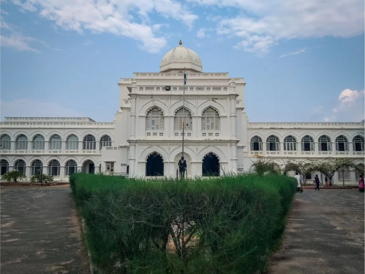 Symmetrical front view of Gandhi Memorial Museum Madurai Tamil Nadu in historic Tamukkam Palace showing white Indo-Saracenic facade central dome arched corridors manicured hedges wide courtyard under partly cloudy blue sky