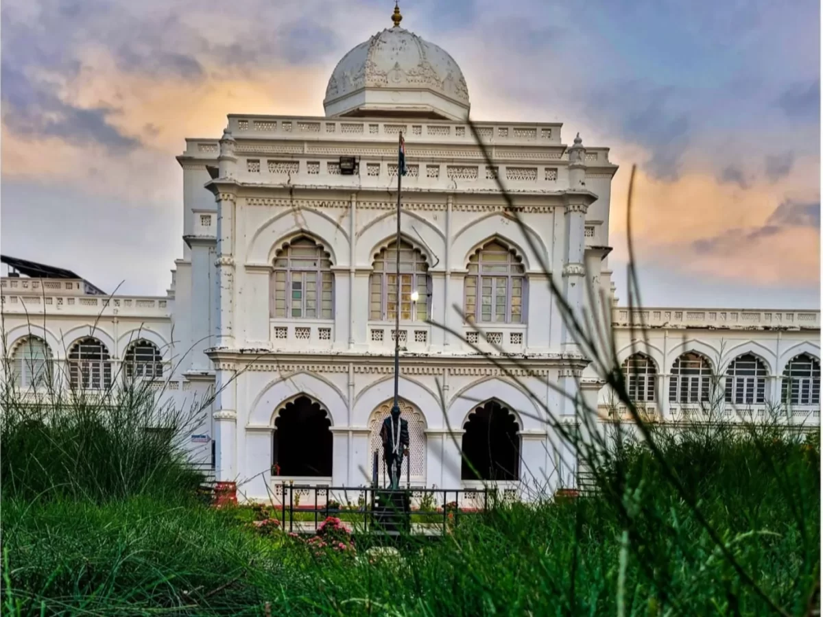 Gandhi Memorial Museum Madurai Tamil Nadu elegant white domed colonial building framed by tall grass foreground Gandhi statue flagpole gardens under golden hour sky, historic freedom tour package