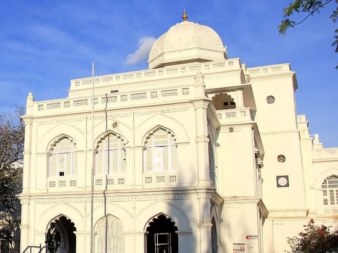 Gandhi Memorial Museum Madurai Tamil Nadu pristine white Indo-Saracenic domed building with ornate arches flagpole surrounded by lush greenery under clear blue sky, essential history tour package.