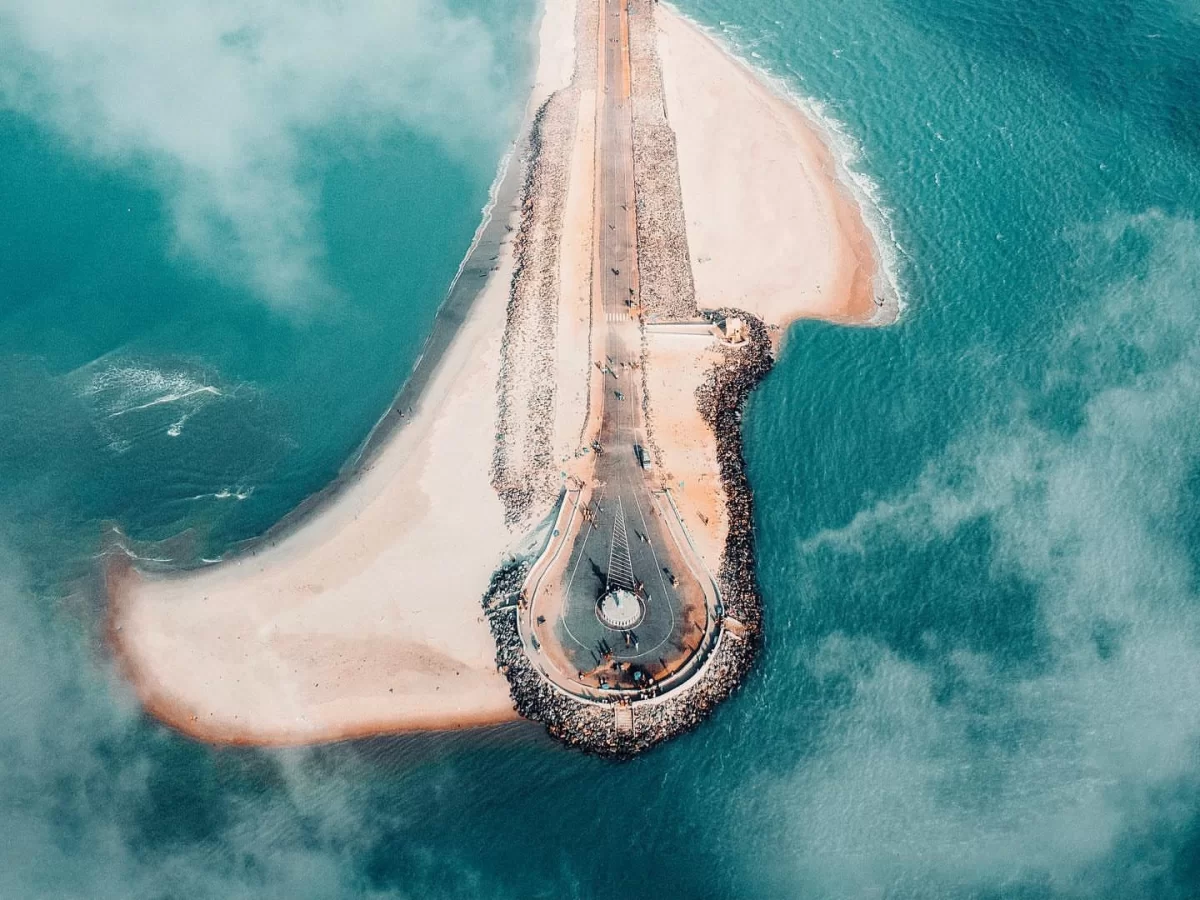 Aerial Pamban road at Arichal Munai Beach Dhanushkodi misty skies, curving sandbar turquoise seas rock jetties; perfect Rameswaram Dhanushkodi tour package.