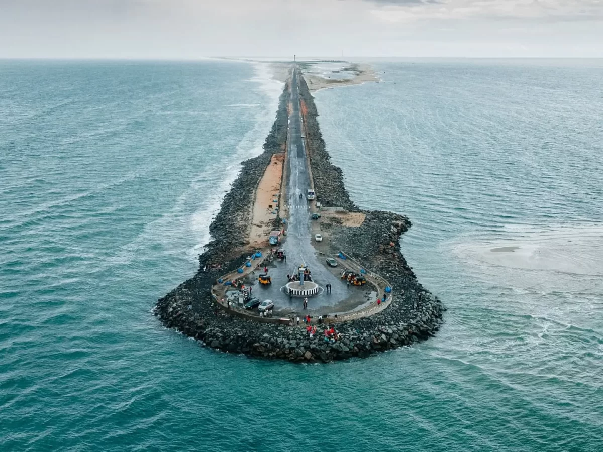 Aerial construction Pamban road at Arichal Munai Beach Dhanushkodi misty day, sandbar turquoise seas vehicles workers jetties; perfect Rameswaram Dhanushkodi tour package.