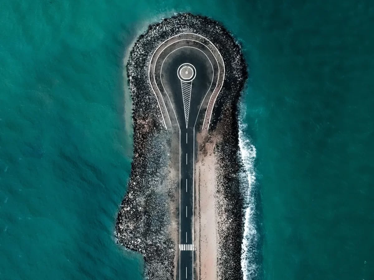 Aerial roundabout Pamban road at Arichal Munai Beach Dhanushkodi misty day, sandbar turquoise seas rock breakwaters; perfect Rameswaram Dhanushkodi tour package.
