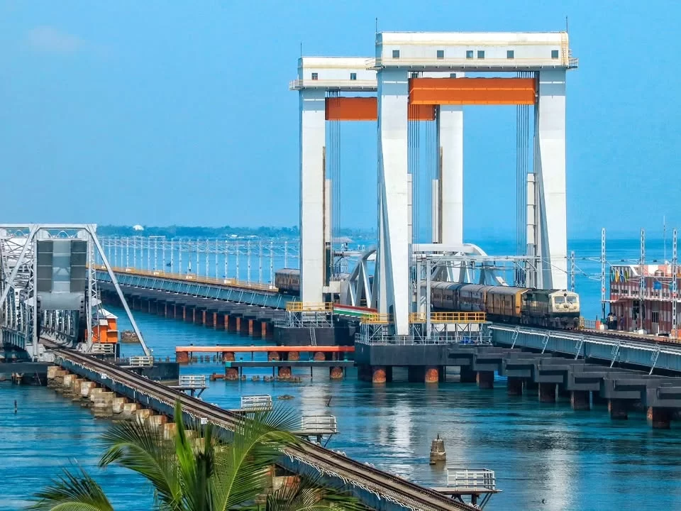 Train on new Pamban Bridge in Rameswaram during clear day, featuring orange cranes, old bridge, sea views, perfect Rameswaram tour package.