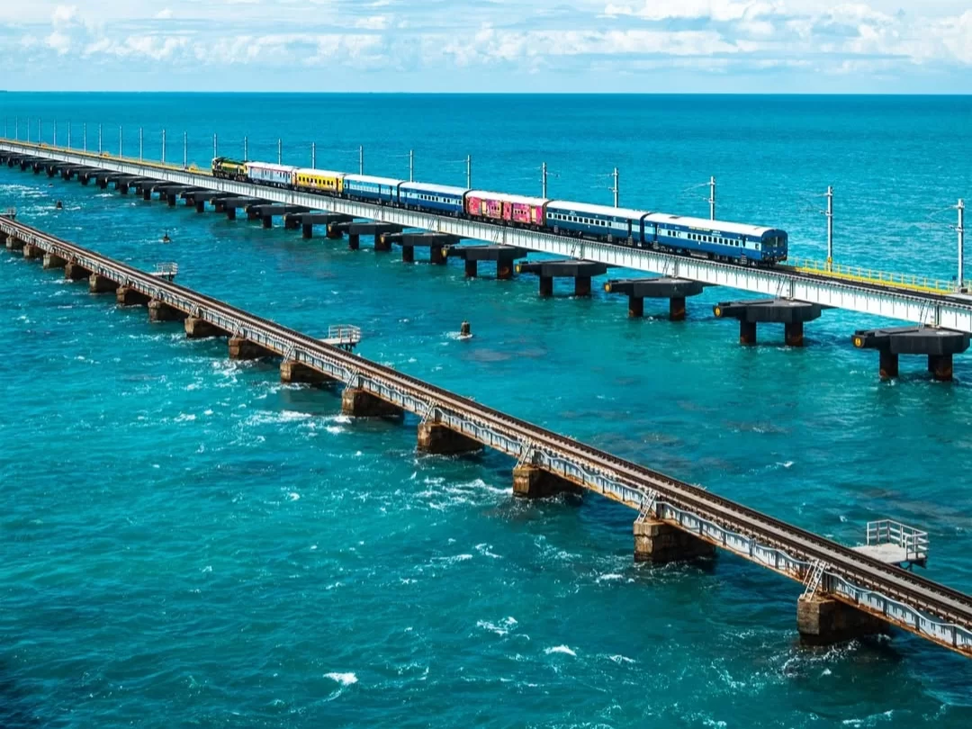 Trains crossing parallel Pamban Bridges in Rameswaram over turquoise sea, featuring pillars and waves, perfect Rameswaram tour package.