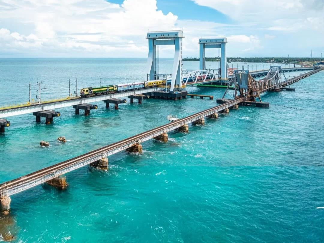 Trains near new Pamban Bridge lift span in Rameswaram under partly cloudy sky, featuring turquoise sea, perfect adventure Rameswaram tour package