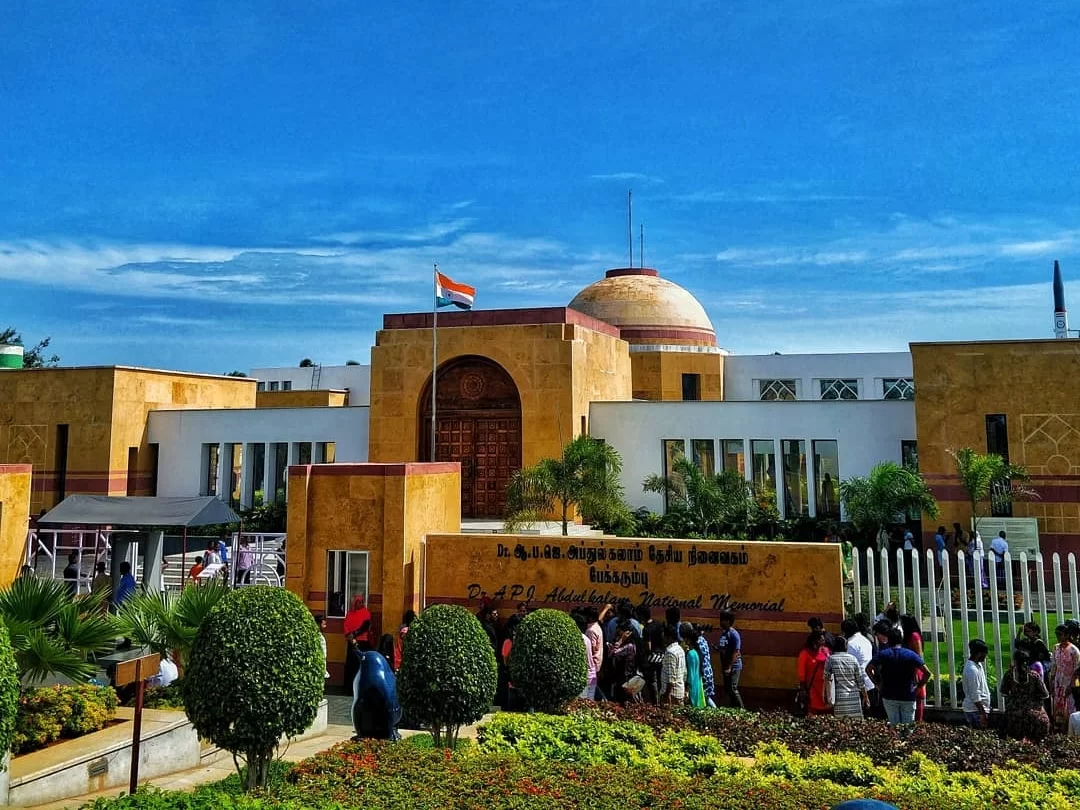 Dr. A.P.J. Abdul Kalam Memorial Pei Karumbu Rameswaram Tamil Nadu India beige sandstone dome building Indian tricolor flag tourists visitors landscaped garden entrance sign Malayalam English sunny partly cloudy skies palm trees hedges, perfect Indian heri