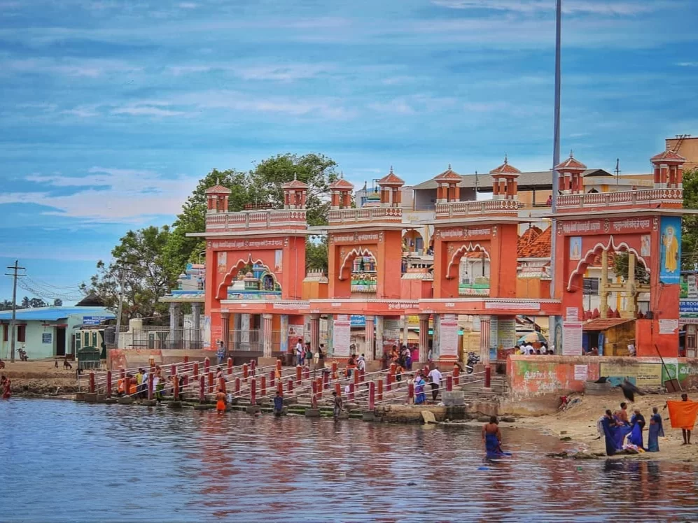 Agni Teertham Rameshwaram Ramanathapuram Tamil Nadu India striking red ornate temple gate towers steps leading serene reflective waters palm trees blue skies pilgrims bathing foreground, perfect Rameswaram spiritual heritage tour package.