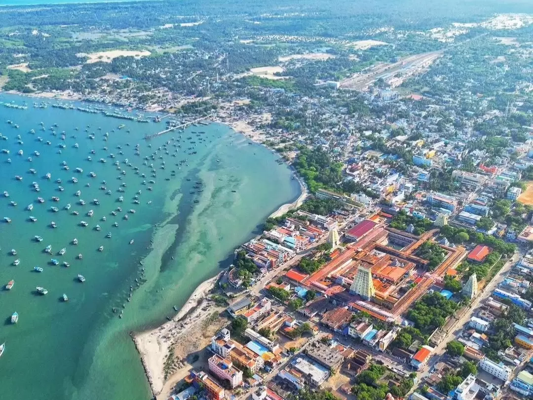 Aerial drone view Pamban Beach Rameshwaram Ramanathaswamy Temple Tamil Nadu India Bay Bengal Arabian Sea fishing boats anchored colorful town buildings shoreline sand sea meeting sky clear sunny day, perfect coastal pilgrimage beach tour package.